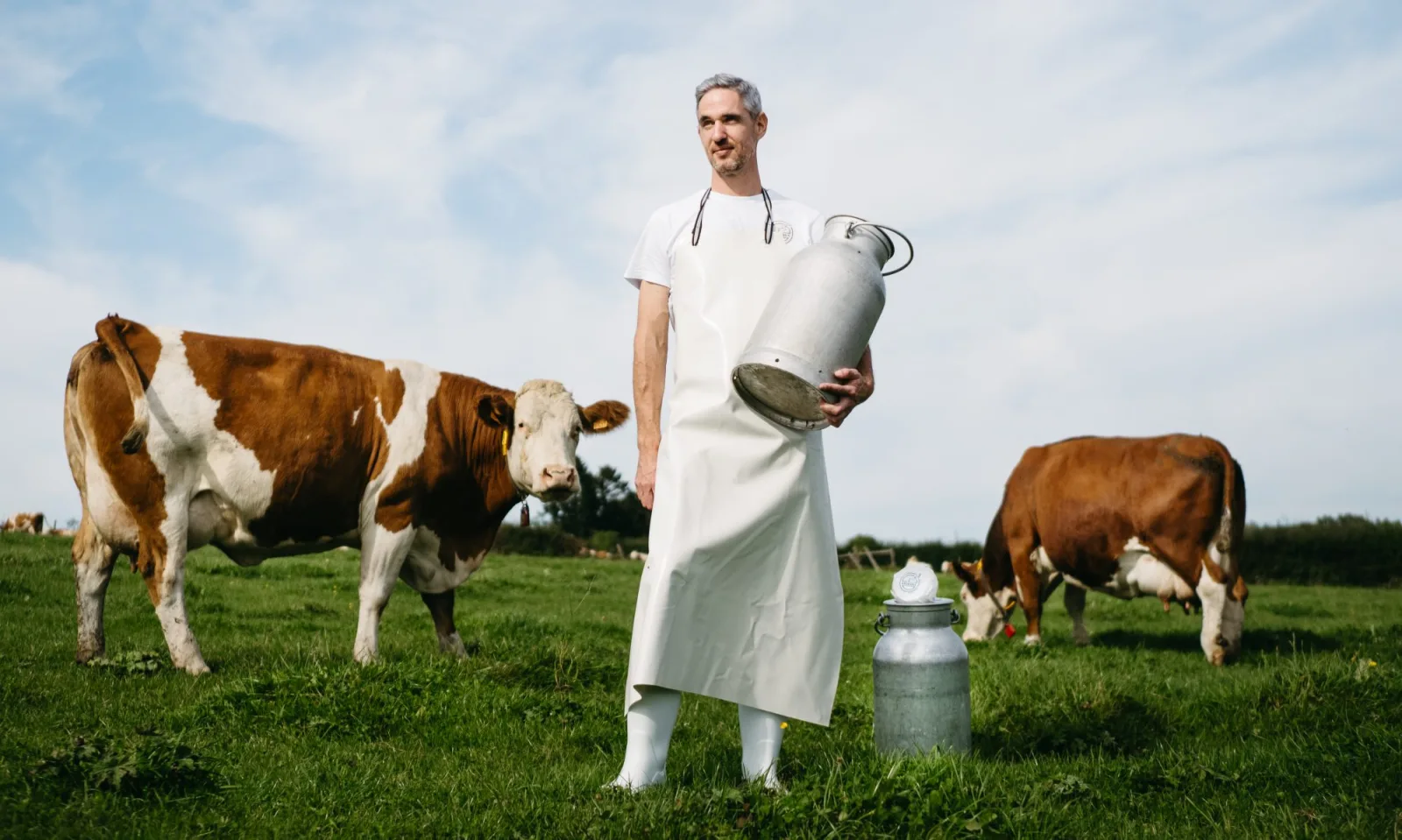 Jürgen Reinertz mit Milchkanne zwischen zwei Kühen auf der Weide